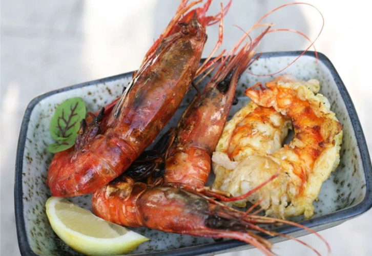 Grilled rock lobster tail and king prawn with lemon wedge on plate