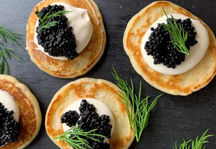 Warm blinis topped with burrata cheese and Royal Baeri caviar on a white plate