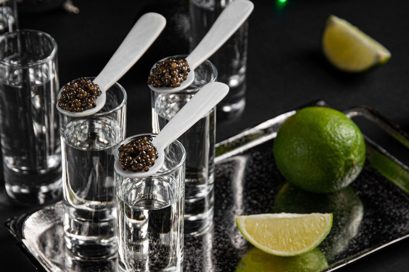 Caviar served on mother of pearl spoons paired with chilled vodka in small glasses on ice