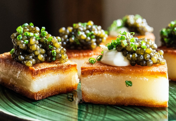Golden potato bites topped with fresh dill and Royal Oscietra caviar on a white plate