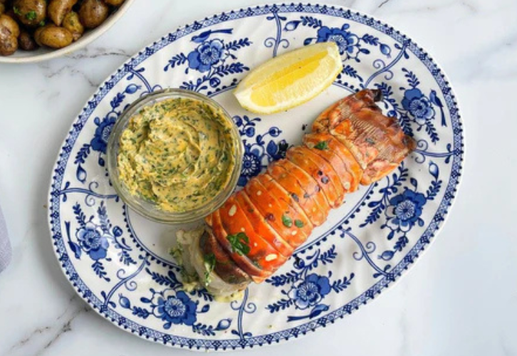 Grilled rock lobster tail served with garlic butter and lemon wedges on a white plate