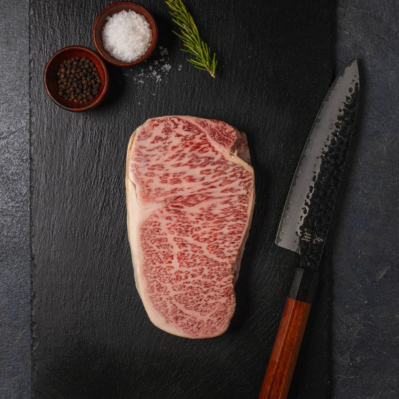 Raw Japanese A5 Wagyu sirloin beside a chef's knife for slicing and serving