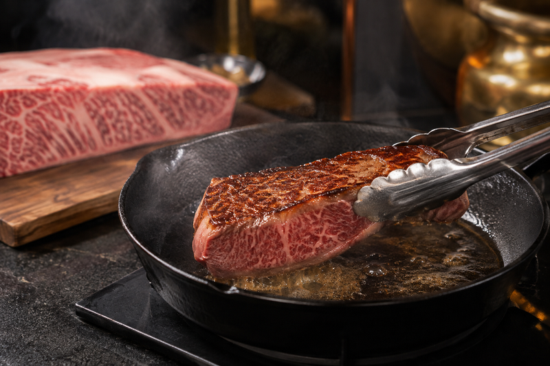 Marbled Japanese-style steak searing in a cast-iron pan for a Kobe Beef cooking guide