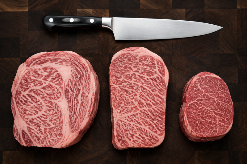 Three marbled beef cuts on a butcher block for a Kobe Beef cuts guide