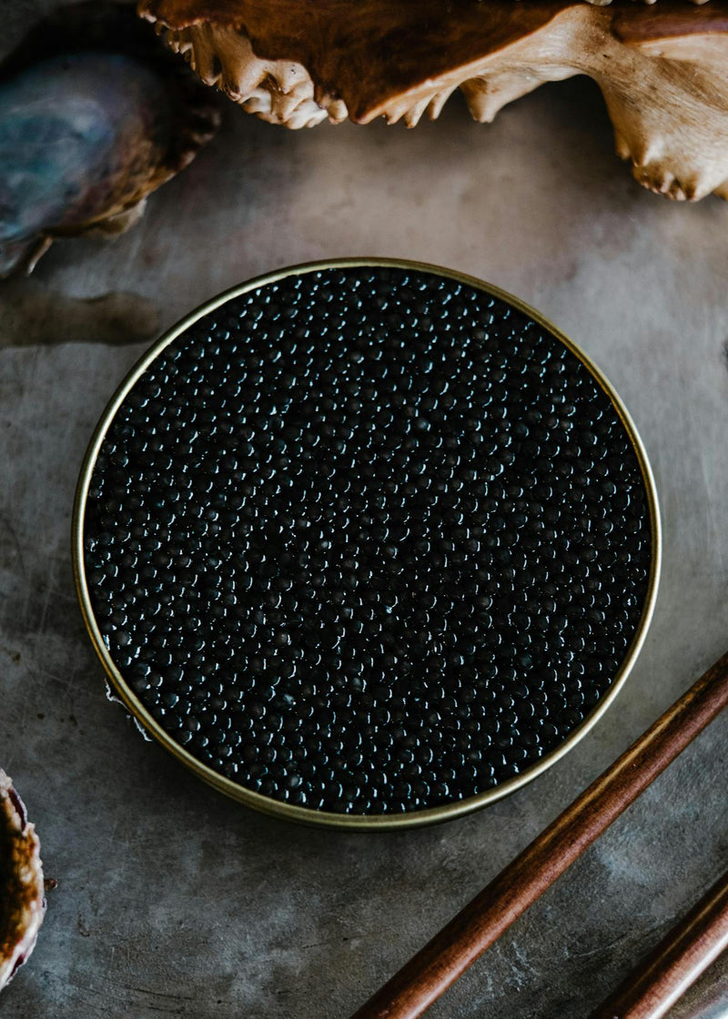 Premium caviar gift set with Oscietra and Baerii tins, mother-of-pearl spoons, and blinis on white marble background