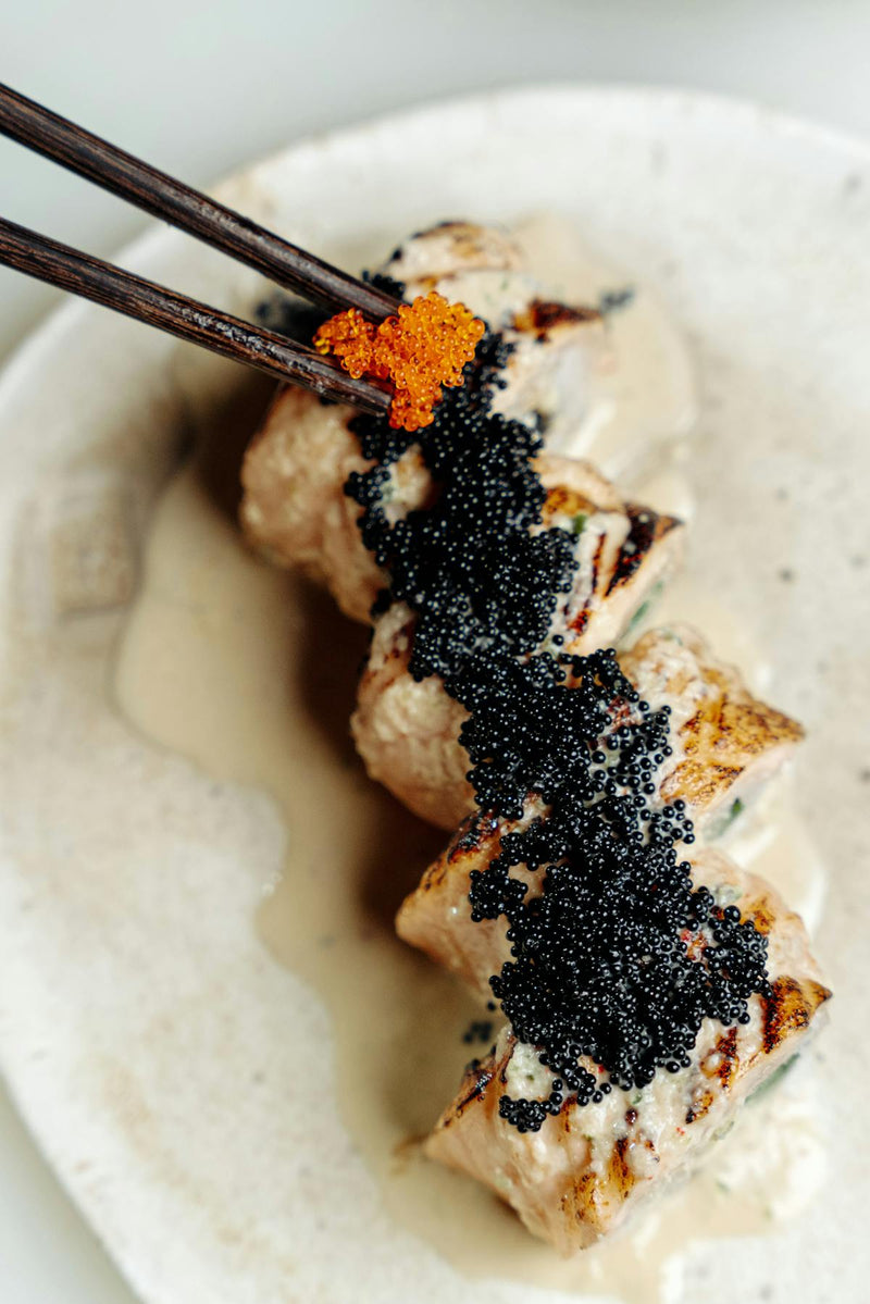Marble board with classic caviar accompaniments including blini, creme fraiche, chopped egg, chives, and open tin of caviar