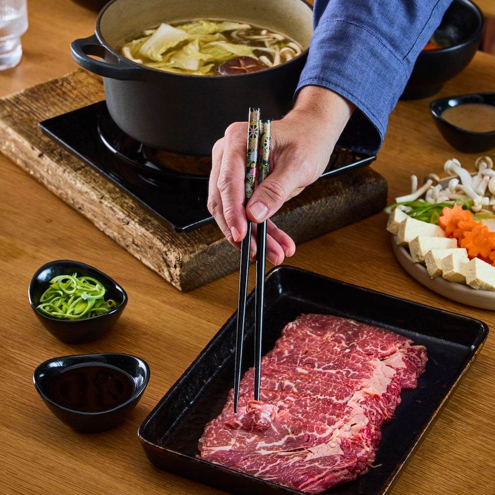 British Wagyu Beef thinly sliced marbled raw beef on black tray with dipping sauces and vegetables for hot pot cooking