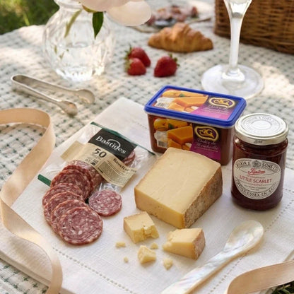Summer picnic hamper with cheese, saucisson, strawberry conserve and toast on a board