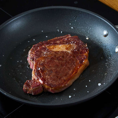 Wagyu British Beef Ribeye Steak with a browned sear and light marbling cooking in a black frying pan with salt flakes