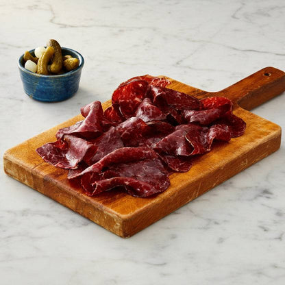 Thinly sliced Wagyu British Beef bresaola with rich marbling, garnished with rosemary sprigs and scattered peppercorns on a slate board