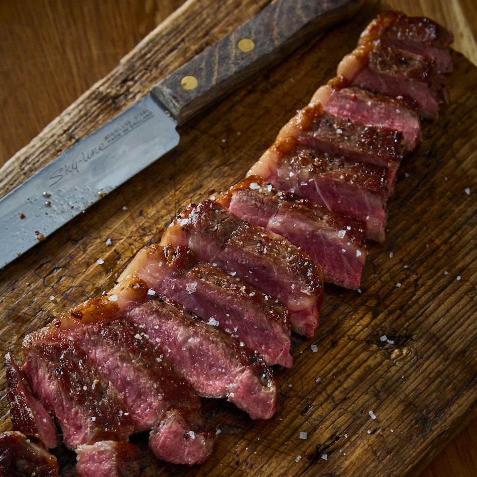 Wagyu British Beef striploin steak cooked medium-rare with visible marbling, sliced on a wooden board with coarse salt